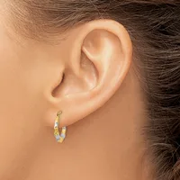 A person wearing small gold and silver two-tone hoop earrings with a textured finish, shown from the side view of their ear and neck.