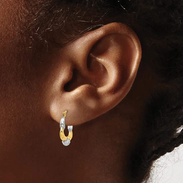 A person wearing a two-tone gold and silver hoop earring with a textured surface on their earlobe.