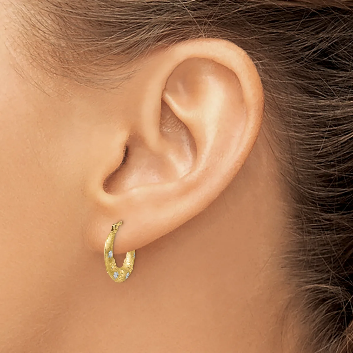 A person wearing a small gold hoop earring with a textured surface is shown in profile, displaying the earring in the pierced earlobe.