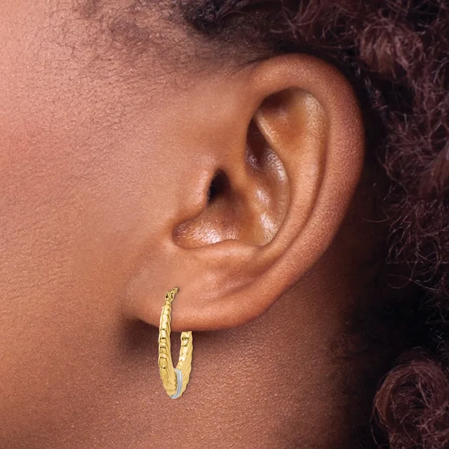 A close-up of a person's ear wearing a textured gold hoop earring with a dimpled or hammered surface finish.
