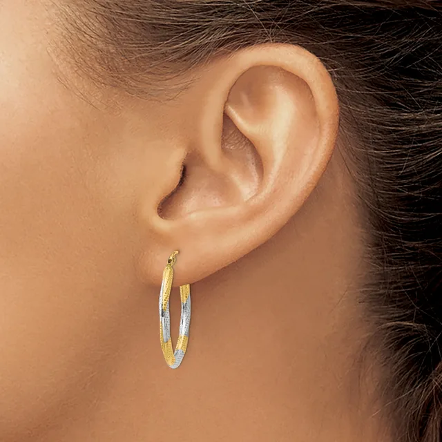 A person wearing two-tone oval hoop earrings with a textured finish, shown from the side profile with dark hair pulled back.