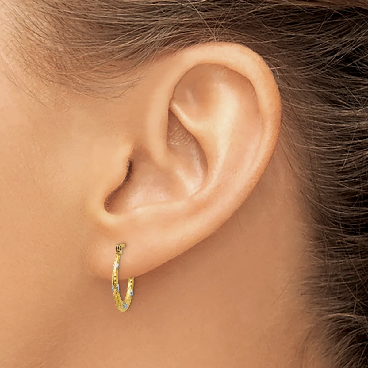 A person wearing a pair of two-tone gold hoop earrings, shown from the side profile of their ear and upper neck.