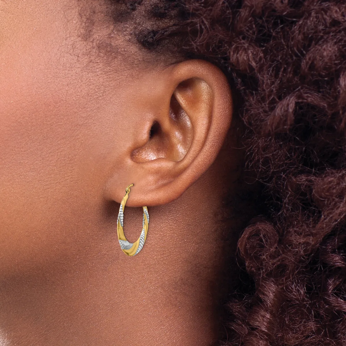 A person wearing two-tone textured hoop earrings with gold and silver finish, shown from the side profile.