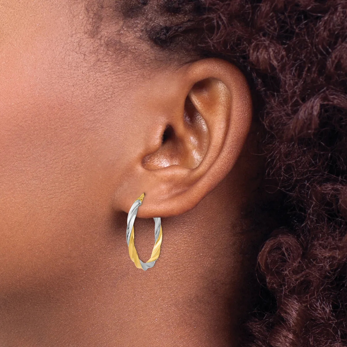 A person wearing two-tone hoop earrings with a silver outer surface and gold inner surface, shown from the side profile near their ear.