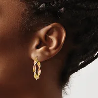 A twisted gold hoop earring hangs from the earlobe of a person with deep brown skin and black curled hair.