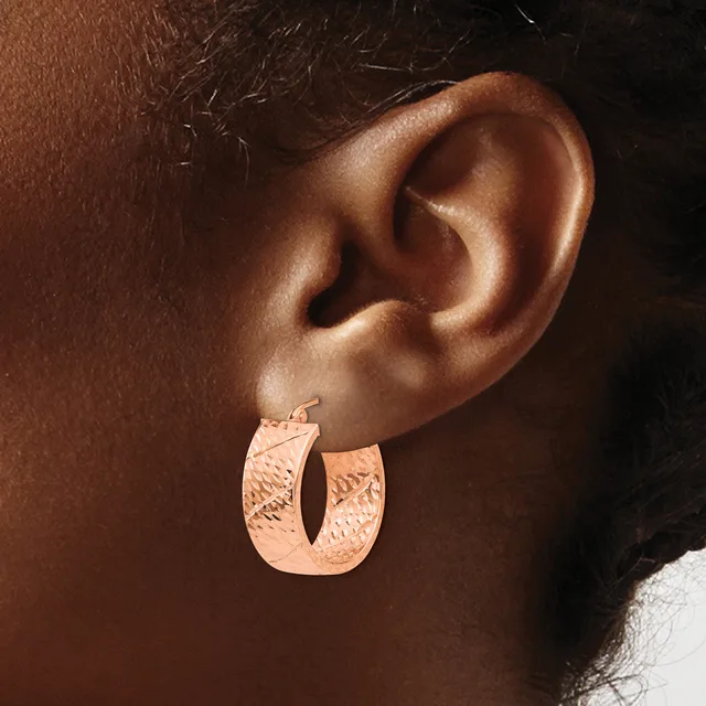 Rose gold textured hoop earrings with a curved rectangular shape worn on a person's ear.