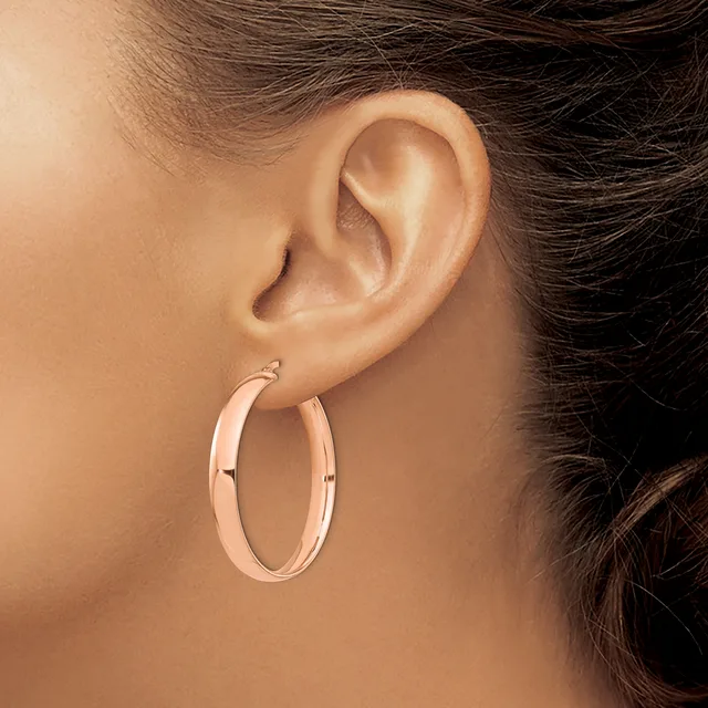 A person wearing rose gold hoop earrings with a polished finish and small hinged closures, shown from the side profile view of their ear.