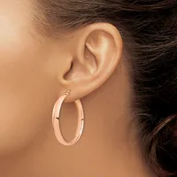 A person wearing rose gold hoop earrings with a polished finish and small hinged closures, shown from the side profile view of their ear.