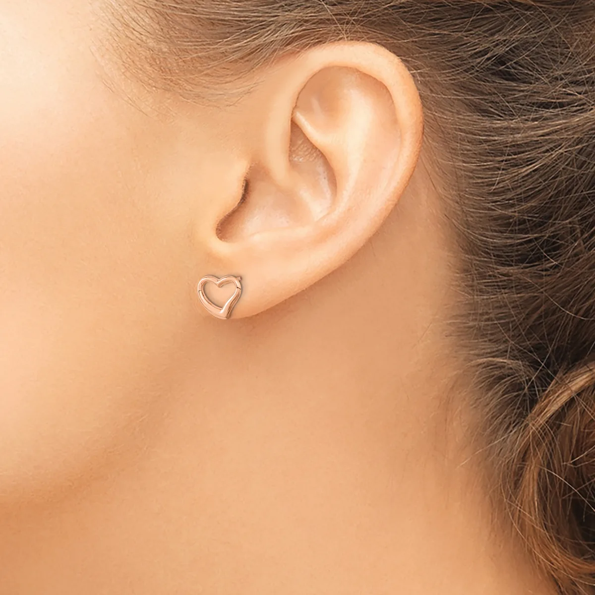 A person wearing a small silver heart-shaped stud earring in their earlobe, shown in profile with brown hair pulled back.
