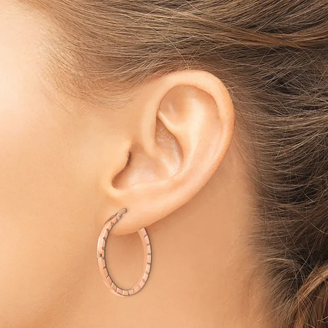 A woman wearing a textured oval hoop earring in rose gold, shown from the side view of her ear and neck.