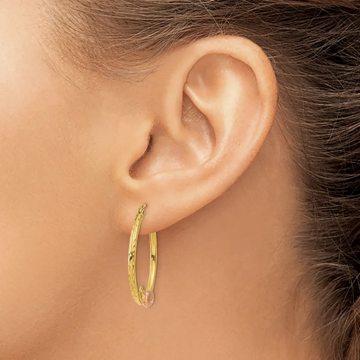 A person wearing gold hoop earrings with a textured surface, shown from the side profile of their head and ear.