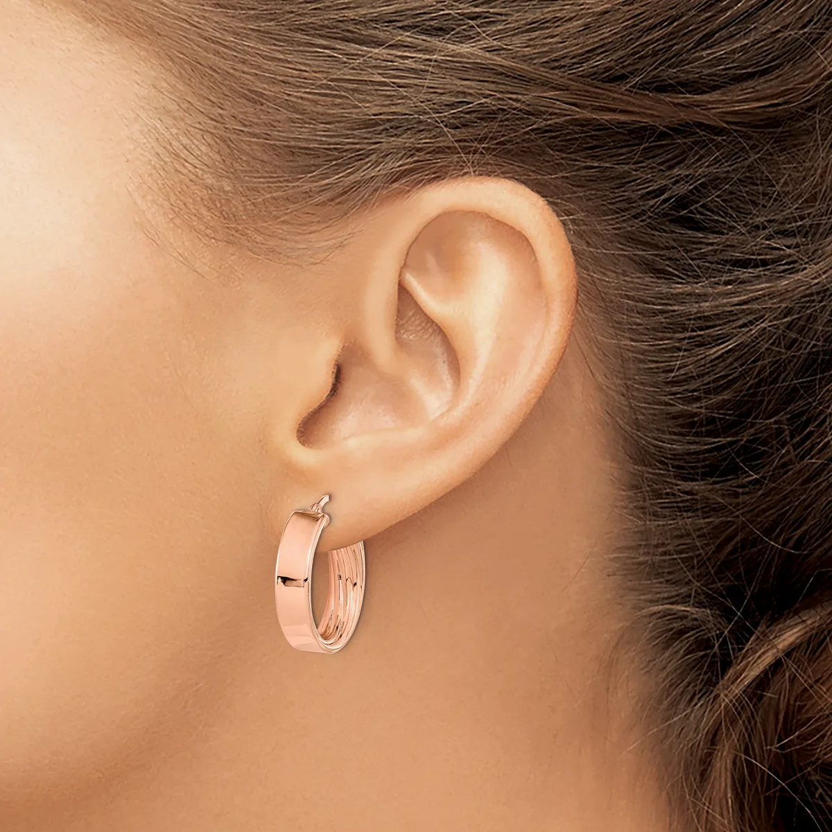A person wearing rose gold hoop earrings with a polished finish, shown from the side profile near their ear.