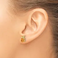 A person wearing a small gold earring shaped like an apple with an amber-colored stone body and green leaf detail on the earlobe.