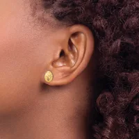 A person wearing a small gold teardrop-shaped stud earring with a textured surface in their earlobe, shown in profile.