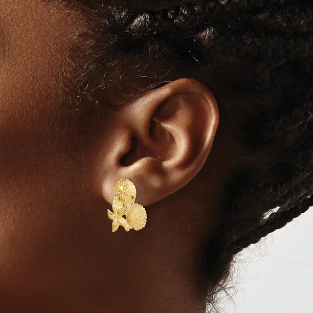 A person wearing a gold-colored butterfly-shaped earring with textured wings on their earlobe.