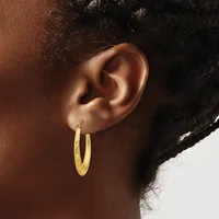 A person wearing a pair of gold hoop earrings with a textured finish, shown from the side profile of their head and neck.