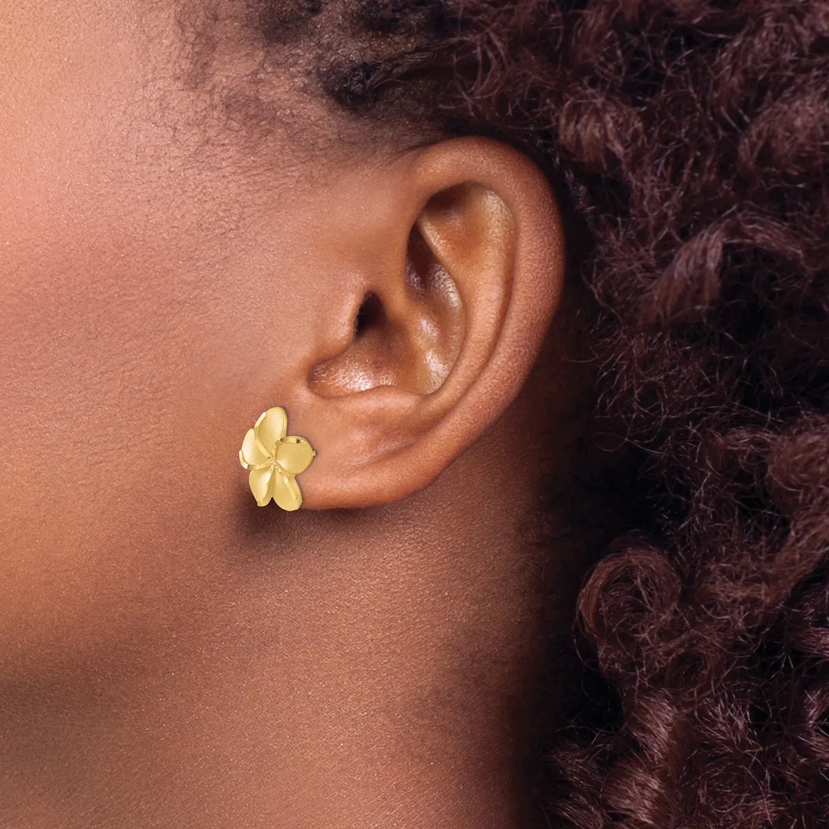 A person wearing a gold-colored flower-shaped stud earring with five petals on their earlobe.
