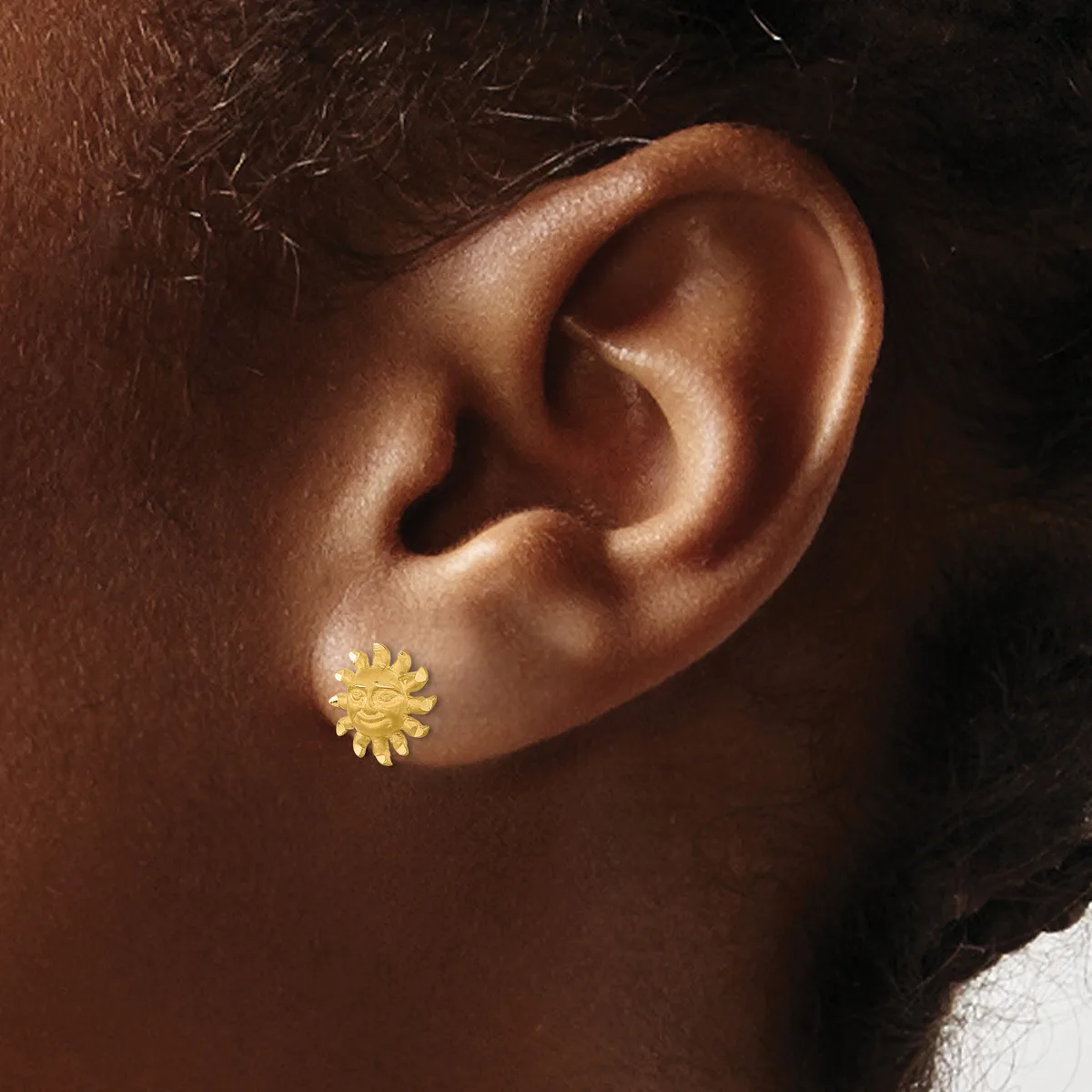 A gold-colored flower-shaped stud earring with multiple petals worn on a person's earlobe against a dark background.