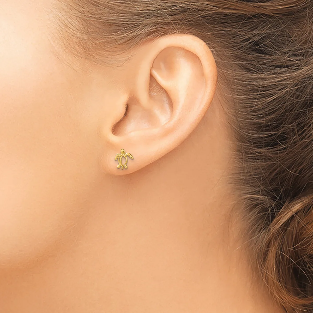 A person wearing a small gold stud earring with an ornamental design in their earlobe, shown in profile view.