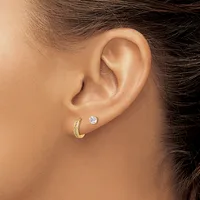 A person wearing a gold hoop earring with diamond accents on one ear and a round diamond stud earring on the other ear.