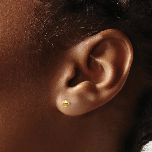 A small gold ball stud earring in a pierced earlobe, shown in close-up profile view against warm brown skin tones.