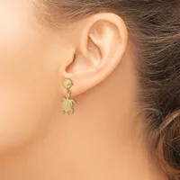 A person wearing a gold turtle-shaped dangle earring with a textured finish on a post and clutch back.