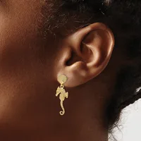 A gold seahorse-shaped dangle earring with a textured stud top worn on a person's ear.