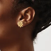 A close-up of a person's ear wearing a gold ship wheel-shaped earring with small beaded details along the bottom edge.