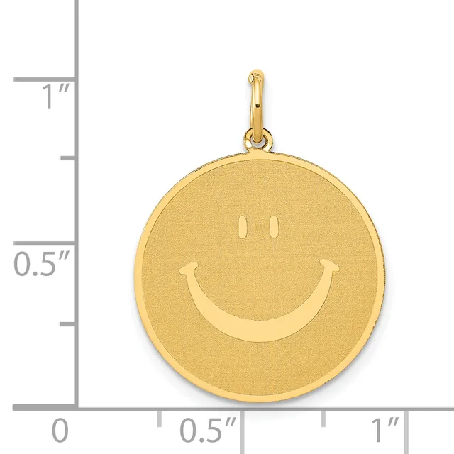 A gold circular pendant with a smiley face design shown next to a ruler for scale, measuring approximately one inch in diameter.
