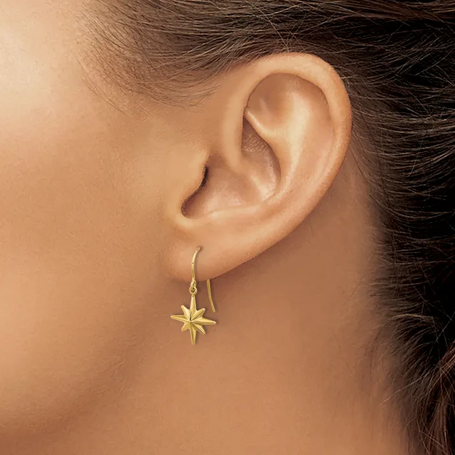 A person wearing gold star-shaped drop earrings on fish hook wires, shown from the side profile of their ear and neck.
