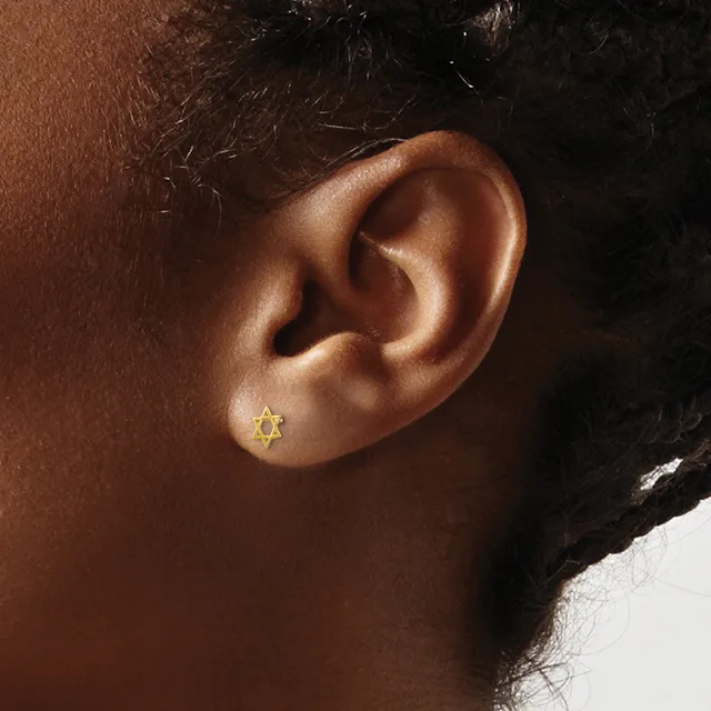 A gold Star of David stud earring worn in the earlobe of a person with medium brown skin tone.