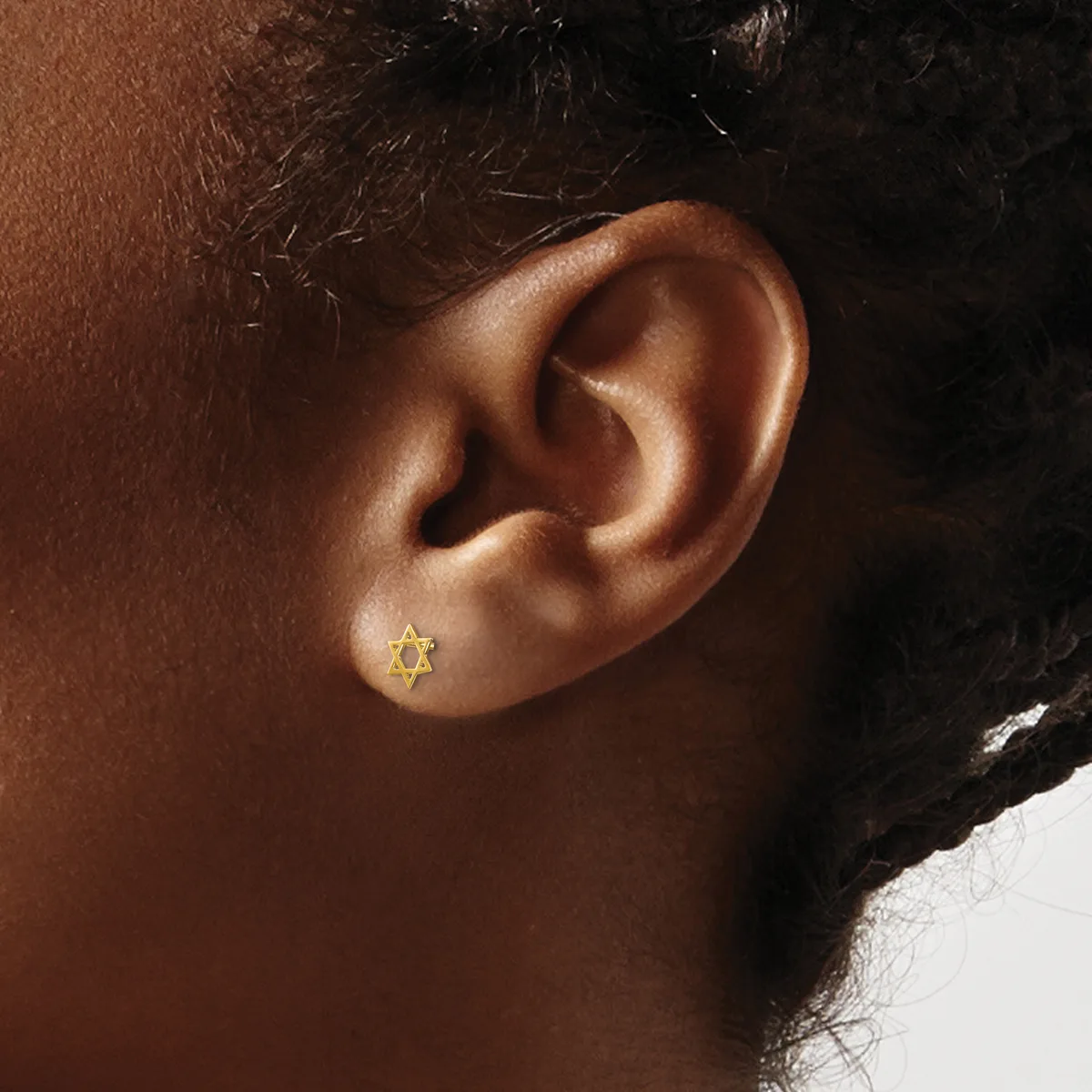 A gold Star of David stud earring worn in the earlobe of a person with medium brown skin tone.