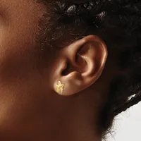 A close-up side view of a person's ear wearing a small gold-colored heart-shaped stud earring.