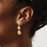 A woman wearing gold-toned drop earrings with textured spherical and shell-shaped pendants, shown from the side profile.