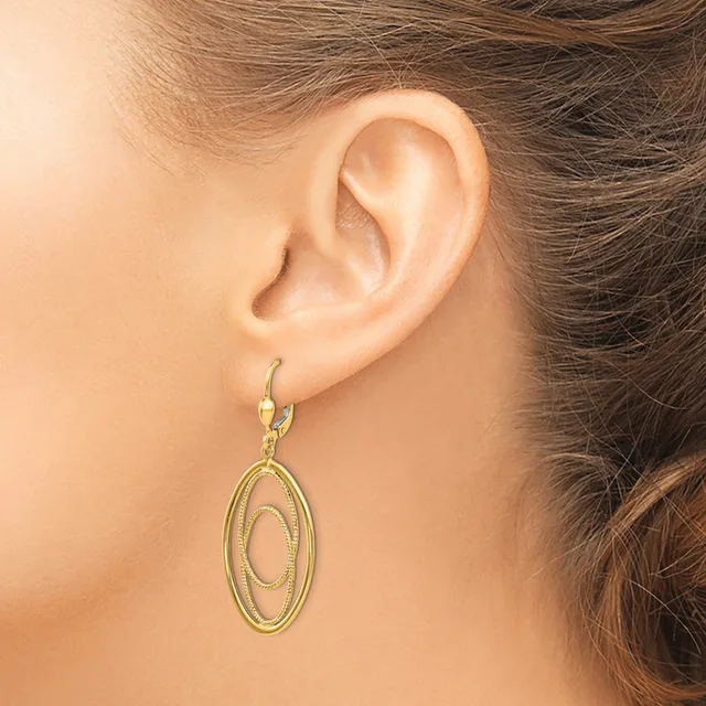 A woman wearing a gold-toned oval dangle earring with concentric oval designs, shown from the side view of her ear and neck.