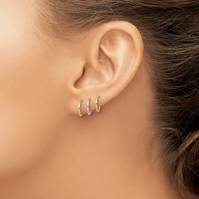Close-up of a person's ear wearing three small hoop earrings in gold, silver, and rose gold finishes.