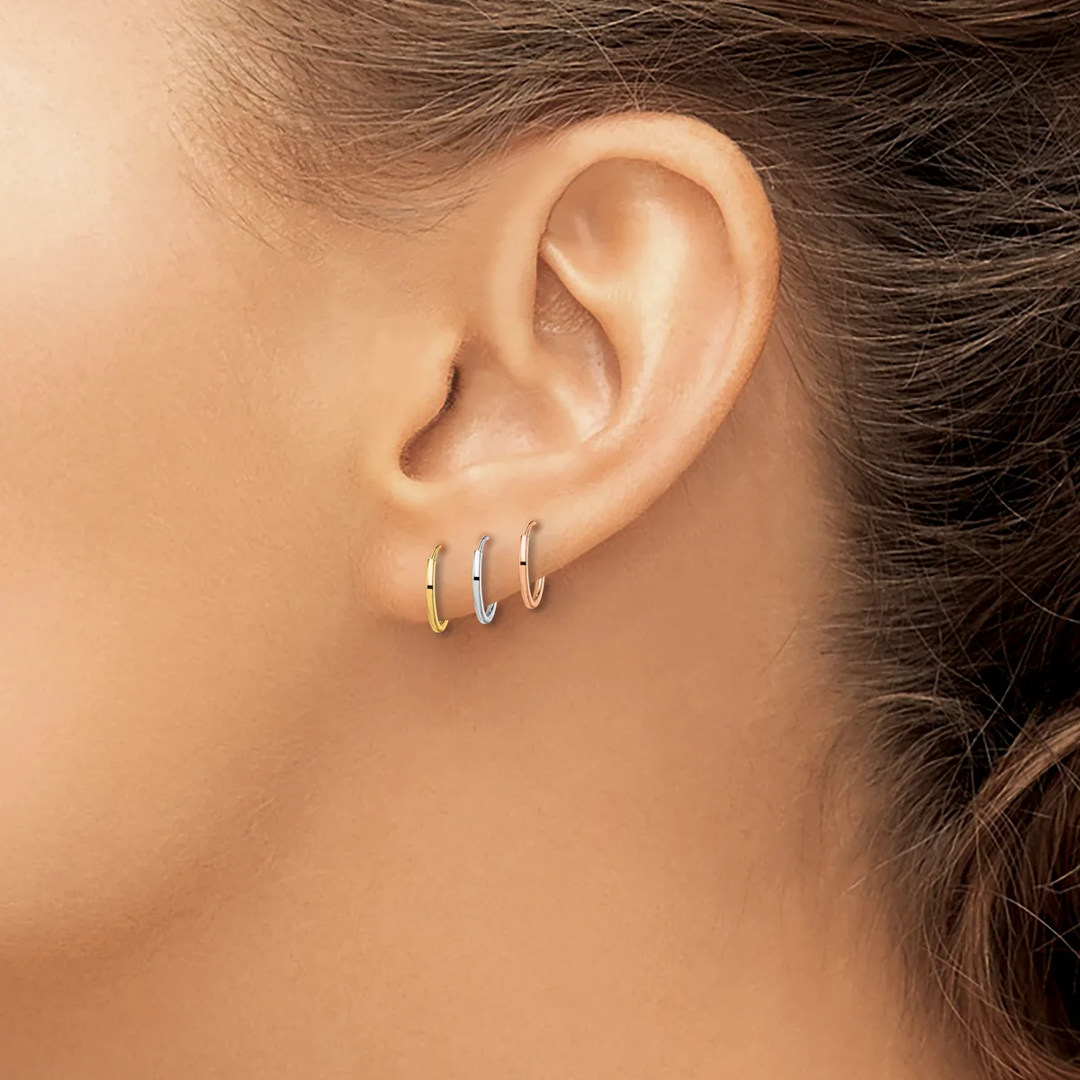 Close-up of a person's ear wearing three small hoop earrings in gold, silver, and rose gold finishes.