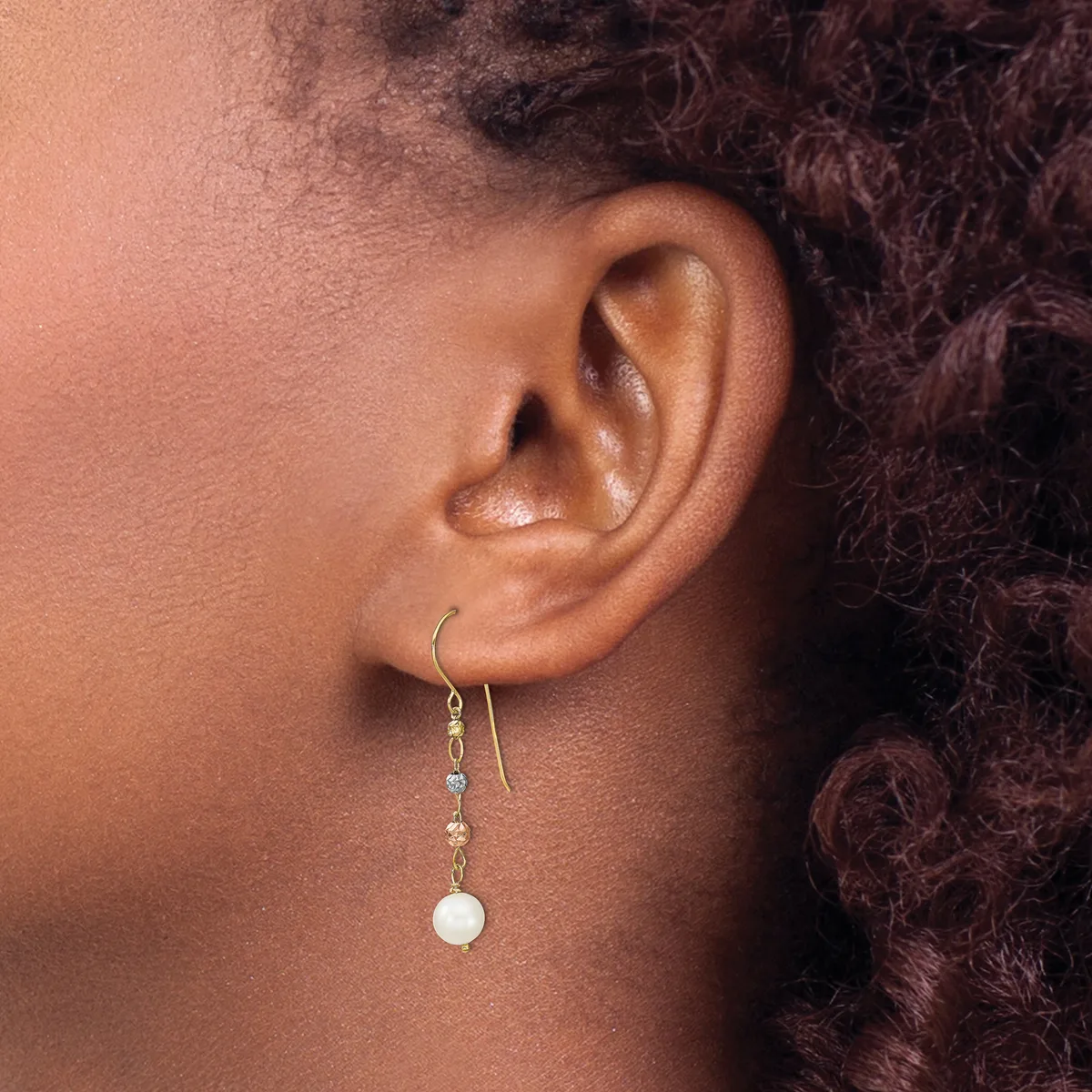 A person wearing a dangling earring with a white pearl drop and small beads on a wire hook, shown from the side profile.
