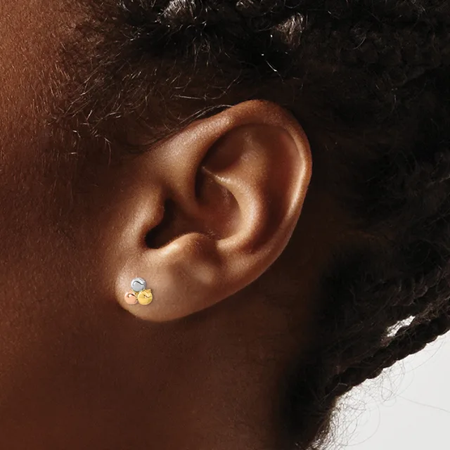 A close-up view of a person's ear wearing a pair of small stud earrings with yellow and clear gemstones.