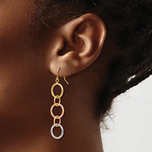 A person wearing gold-toned drop earrings with three linked circular rings hanging from hook-style ear wires.