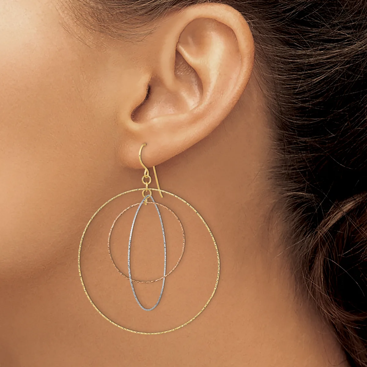 A woman wears a dangle earring made of nested wire circles in mixed metals, suspended from a hook through her earlobe.