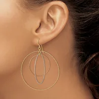 A woman wears a dangle earring made of nested wire circles in mixed metals, suspended from a hook through her earlobe.