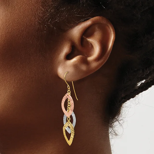A person wearing multi-toned gold drop earrings with interlocking leaf-shaped links and textured surfaces, shown from the side profile.