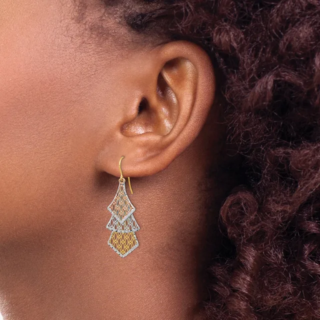 A person wearing a teardrop-shaped filigree earring with two-tone metalwork in gold and silver tones, suspended from a curved ear wire.