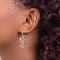 A person wearing a teardrop-shaped filigree earring with two-tone metalwork in gold and silver tones, suspended from a curved ear wire.