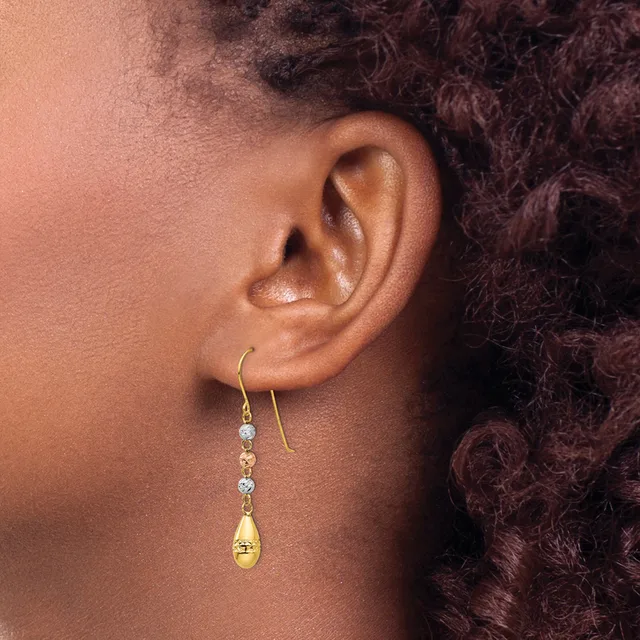 A person wearing gold drop earrings with light blue gemstones and a gold teardrop charm, shown from the side view against dark curly hair.