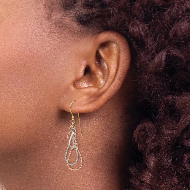 A person wearing a teardrop-shaped dangle earring with textured silver-toned metal and a gold-toned ear wire.