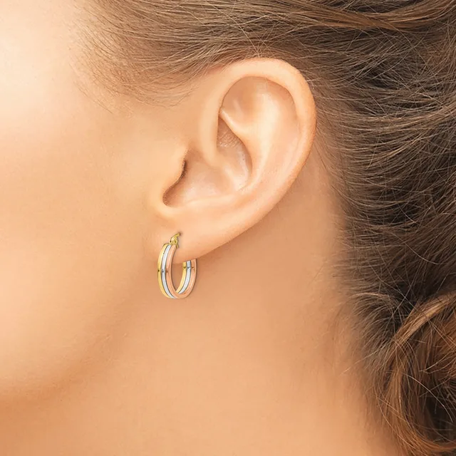 A woman wearing small triple-band hoop earrings in silver-toned metal, shown from the side profile of her ear and neck.
