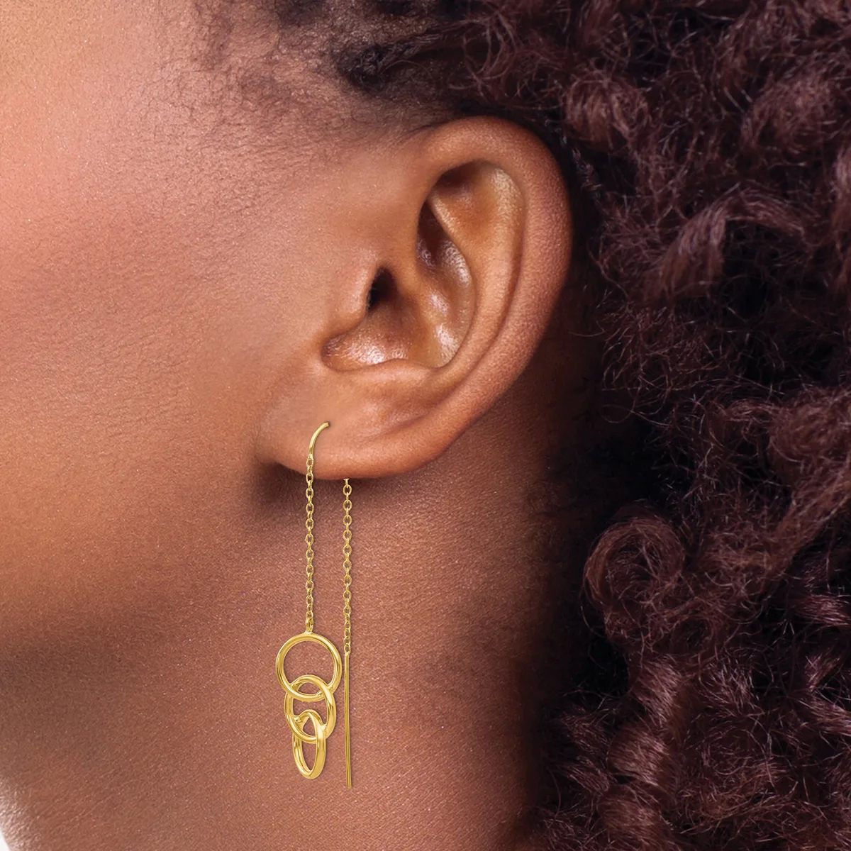 Gold chain threader earrings with linked oval rings hanging from the earlobe of a person with dark curly hair.