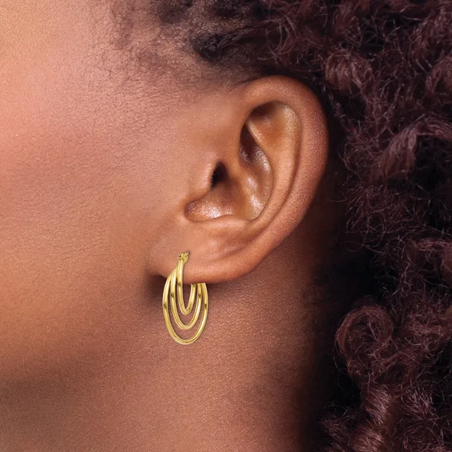 A close-up side view of a person's ear wearing a pair of gold-toned nested oval hoop earrings.